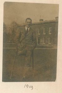 Lionel Whitby on crutches standing in front of the East Range at Downing, 1919